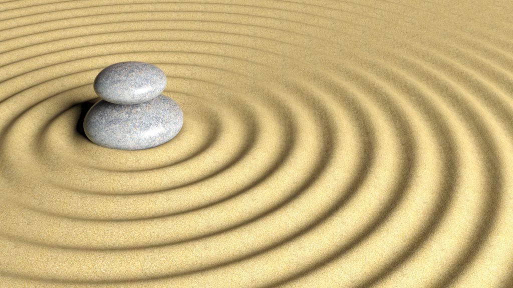 Balancing Zen stones stack from large to small on sand with circular ripples.